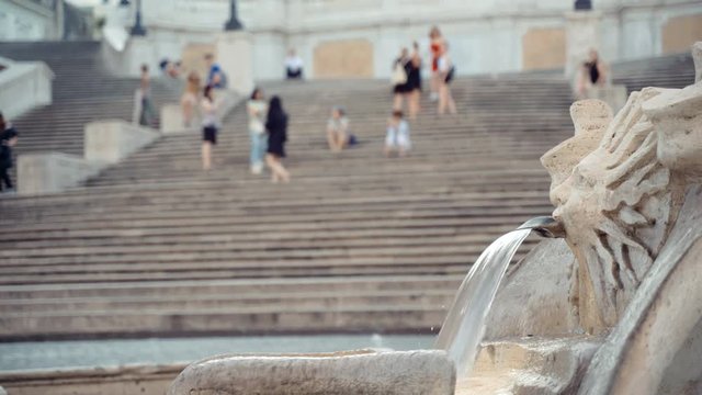 Interesting marble monument in form of someone's head is a famous Roman fountain located in front of the Spanish Steps. Water streaming on the background of Roman sightseeing. People visiting square