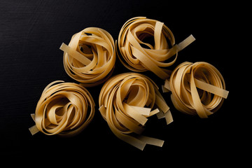 Raw tagliatelle pasta on black background close up