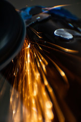 Worker cutting, grinding and polishing motorcycle metal part with sparks indoor workshop. Super macro close-up. 