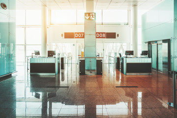 Wide-angle view of empty gates of a modern airport terminal with computer monitors on the counter desks, information screens on the top and the boarding corridors behind, to the airplane