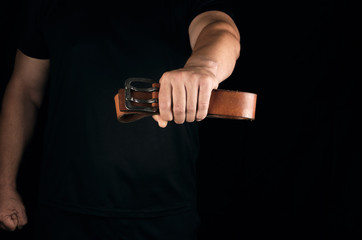 man in black clothes is holding a brown leather belt with a buckle