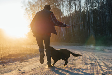 man with active happy black dog playing on the road forest park during sunset or sunrise