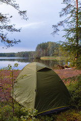 Camping tourism and a green tent near a picturesque lake outdoor. Summer evening sunset sky. Camping and travel concept.