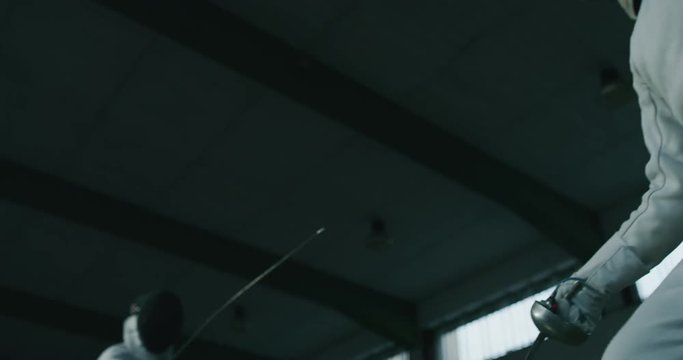 Cinematic slow motion shot of two professional young people is practising assaults of fencing with masks and rapiers in a gym.