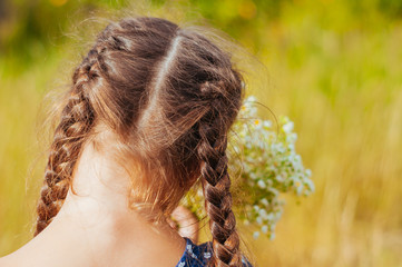 Little girl gathers a bouquet of wild flowers on a summer day in the field, back