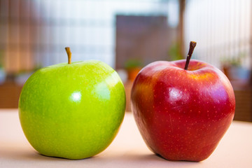 A red apple and a green apple with a garden in the background