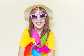 The child is holding a windmill. Little girl in a yellow T-shirt and straw hat.