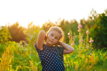 little adorable girl in a field at sunset spread her arms, enjoying