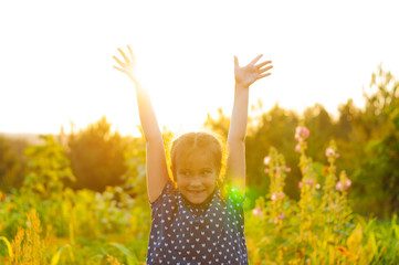 little adorable girl in a field at sunset spread her arms, enjoying