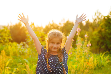 Naklejka na ściany i meble little adorable girl in a field at sunset spread her arms, enjoying