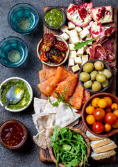 Antipasto. Wine set appetizer. Ham serrano, smoked salmon, dried and fresh tomatoes olive cheese, wine on board. Top view, gray cncrete background