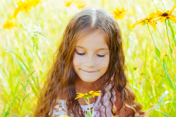 Little girl with long hair in a white dress rejoices in a field with flowers