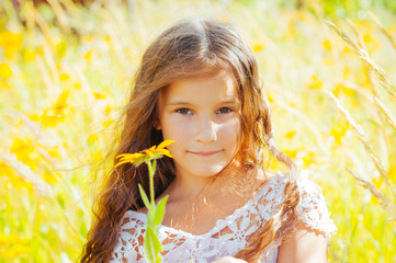 Fototapeta premium Little girl with long hair in a white dress rejoices in a field with flowers
