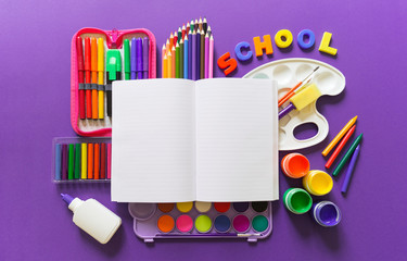 An open notebook lies on a Violet background. Around office supplies are the color of the rainbow.