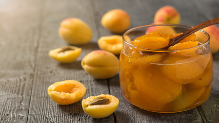 Spoon in a jar of apricot jam and fresh apricots on a wooden table.
