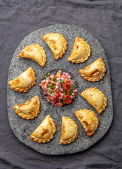 Different little cocktail EMPANADAS on stone plate with tomato sauce and guacamole . Gray background. Latin American and Spanish tipical food