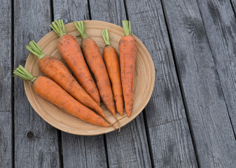 Fresh orange carrots in a wooden plate. On the background of an old wooden table. Summer. Sunny day.