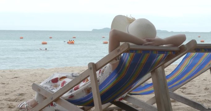 Summer beach vacation concept, Happy young Asian woman with hat relaxing on beach chair and raised hands up.