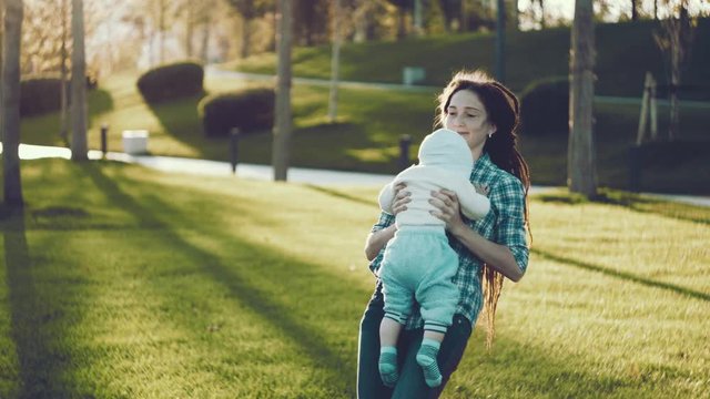 Modern happy mother with baby son in ergo backpack walking in Sunny summer day. Concept of the joy of motherhood