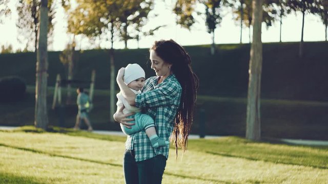 Modern happy mother with baby son in ergo backpack walking in Sunny summer day. Concept of the joy of motherhood