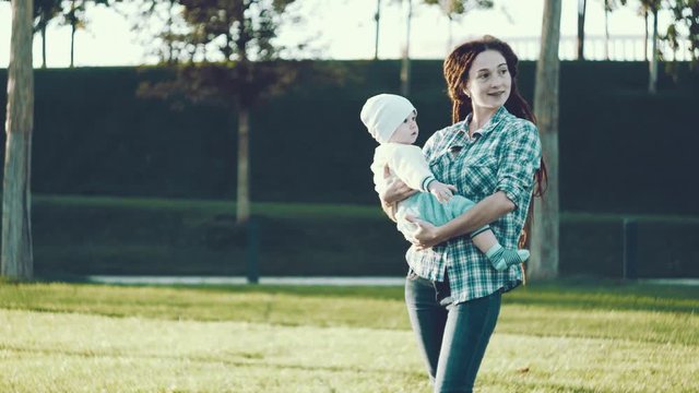 Modern happy mother with baby son in ergo backpack walking in Sunny summer day. Concept of the joy of motherhood