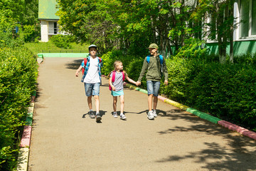 Fototapeta premium Joyful boys and girl brother and sister go to school with school bags. Horizontal frame. Selective focus. Copy space.
