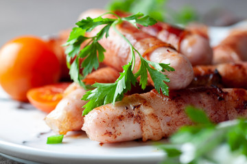 Grilled wrapped bacon sausages on white plate