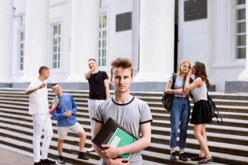 Poor male student is being mocked and sneered by his group mates during break in university campus....