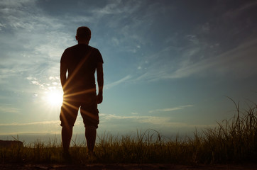 Silhouette of a young man against the backdrop of the setting sun and sky. The concept of...