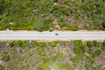 View from above, stunning aerial view of a car that runs along a road flanked by a green forest. Sardinia, Italy.