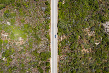 View from above, stunning aerial view of a car that runs along a road flanked by a green forest. Sardinia, Italy.