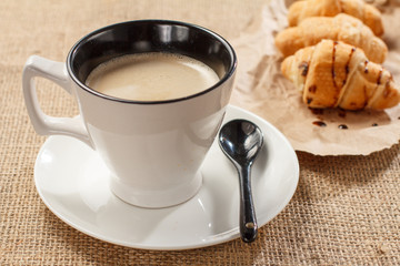 Cup of black coffee with fresh croissants on wrapping paper