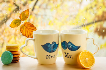 Macaroons, cups with lemon and autumn yellow leaf on window glass with water drops in the blurred background.