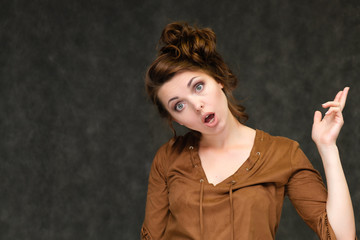 Portrait below breast over gray background of pretty young brunette woman in brown dress with beautiful hair. Standing in different poses, talking, showing with hands, demonstrating emotions.