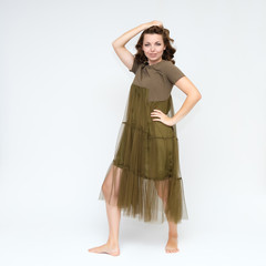 Portrait in full growth on a white background pretty young brunette woman in a green dress with beautiful hair. Standing in different poses, talking, showing hands, demonstrating emotions.