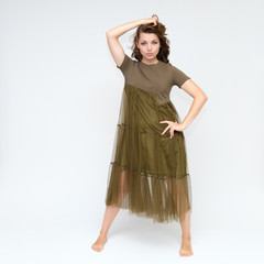 Naklejka premium Portrait in full growth on a white background pretty young brunette woman in a green dress with beautiful hair. Standing in different poses, talking, showing hands, demonstrating emotions.