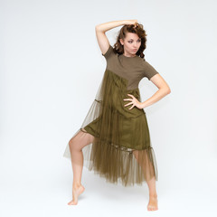 Fototapeta premium Portrait in full growth on a white background pretty young brunette woman in a green dress with beautiful hair. Standing in different poses, talking, showing hands, demonstrating emotions.