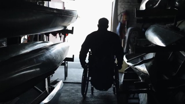 canoe and kayak. A disabled handicapped man leaves the warehouse rides a wheelchair from darkness into the light.