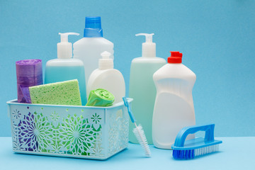 Bottles of dishwashing liquid in basket, sponges and brushes on blue background.