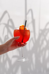 Hand holding Cocktail Aperol spritz in front of illuminated fabric background with shades