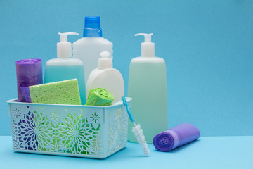 Bottles of dishwashing liquid in basket, sponges and brushes on blue background.