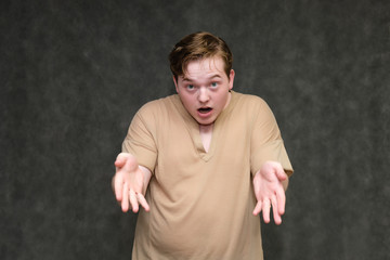 Portrait to the waist on a gray background of a handsome young man in a brown T-shirt. stands directly in front of the camera in various poses, talking, demonstrating emotions.