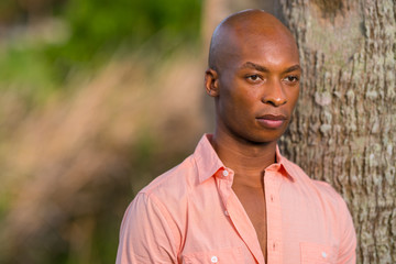 Summertime portrait handsome bald African American man posing by a tree with pink shirt unbuttoned