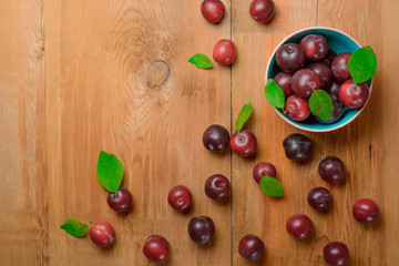 Plums and plate with ripe juicy plums on wooden table. Top view.