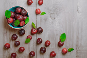 Plate with ripe juicy plums on white wooden table. Top view.