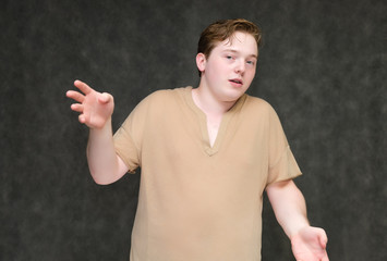 Portrait to the waist on a gray background of a handsome young man in a brown T-shirt. stands directly in front of the camera in various poses, talking, demonstrating emotions.