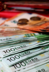 Vertical image of closeup spreading bunches of Euro banknotes with blurry coins and an wallet in background