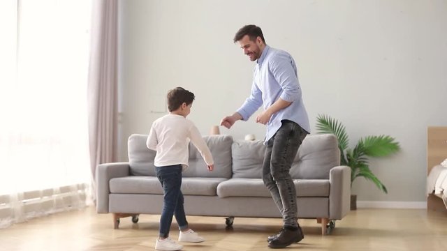 Happy dad and kid son dancing having fun at home