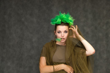 Portrait in lower chest on a gray background of a pretty young brunette woman with a green floral wreath in her hair. Standing in different poses, talking, showing hands, demonstrating emotions.