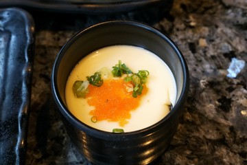 Blurred image of Steamed egg with scallion sliced in big bowl on able in restaurant ready to eat, Kai thoon is Thai traditional (Chawanmushi), Clean food of healthy concept, on dark background